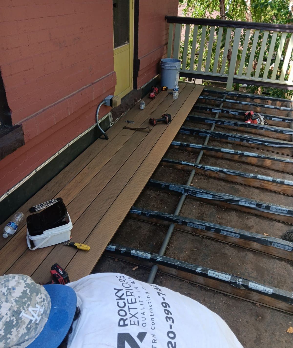 A Rocky Exteriors crew member laying composite deck boards over taped joists on a brick home's porch
