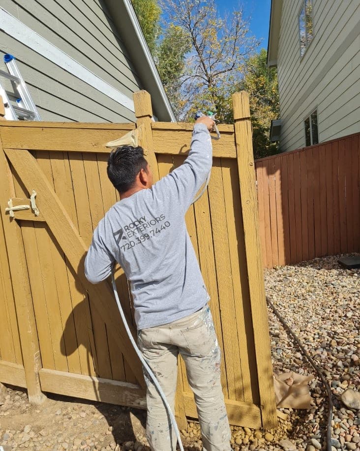 A crew member spraying golden stain on a wooden gate