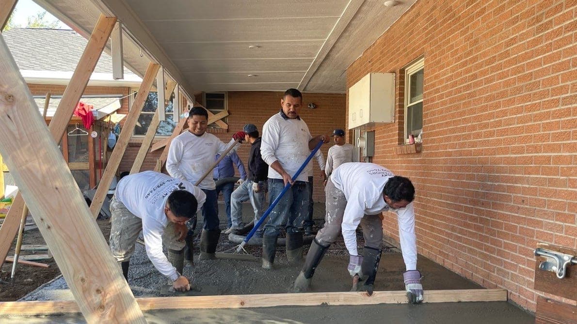 A five-person crew screeding a fresh concrete pour under a covered brick patio