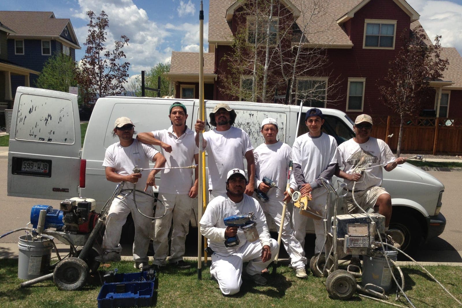 The Rocky Exteriors crew in white work clothes with spray rigs and their van outside a home